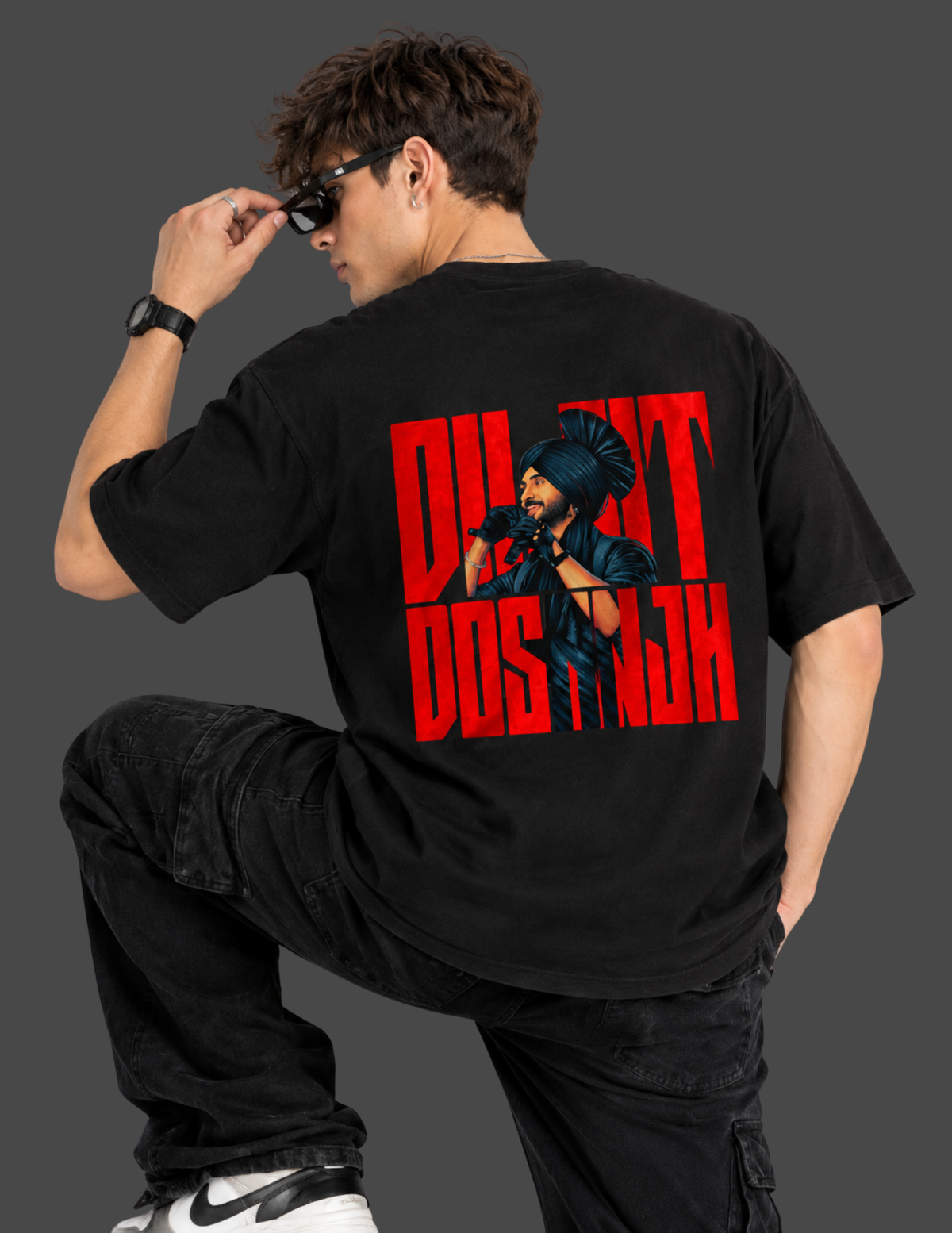 A man wearing a black t-shirt with a large red and black graphic print on the back, posing in black cargo pants against a dark gray background.