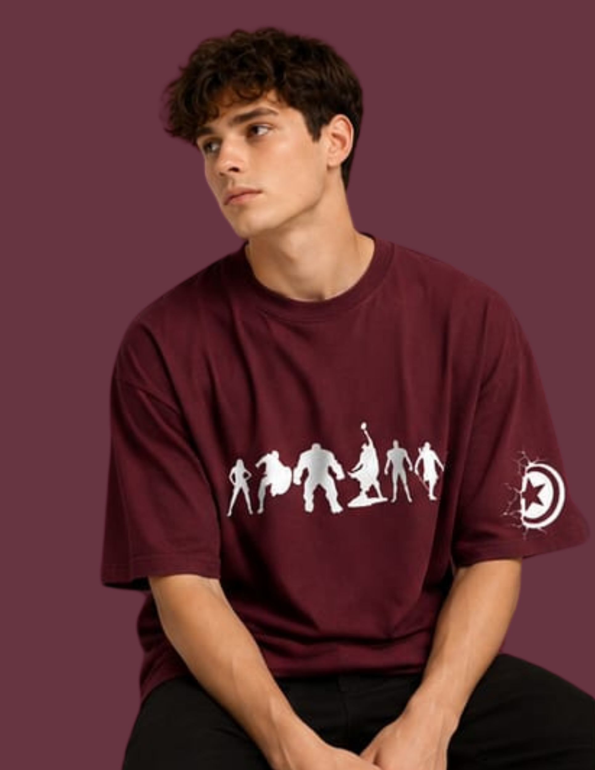 A young man wearing a maroon short-sleeve t-shirt with a white graphic of superhero figures on the front and a Captain America shield logo on the sleeve, set against a solid maroon background.