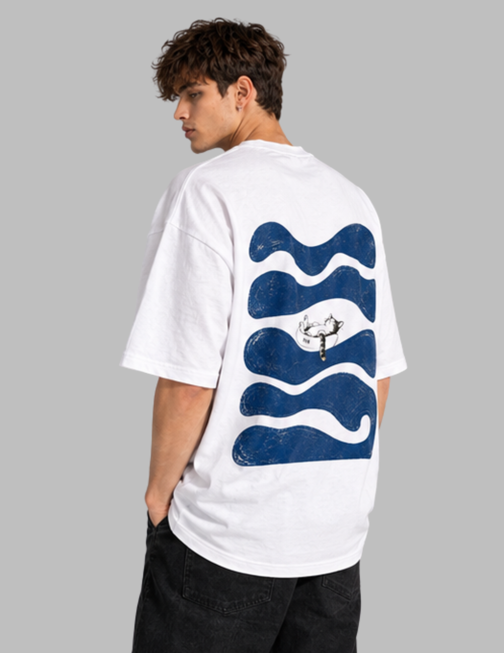 A man wearing a white oversized t-shirt with a large blue wavy graphic and a small deer illustration on the back, shown from a three-quarters back view against a solid gray background.