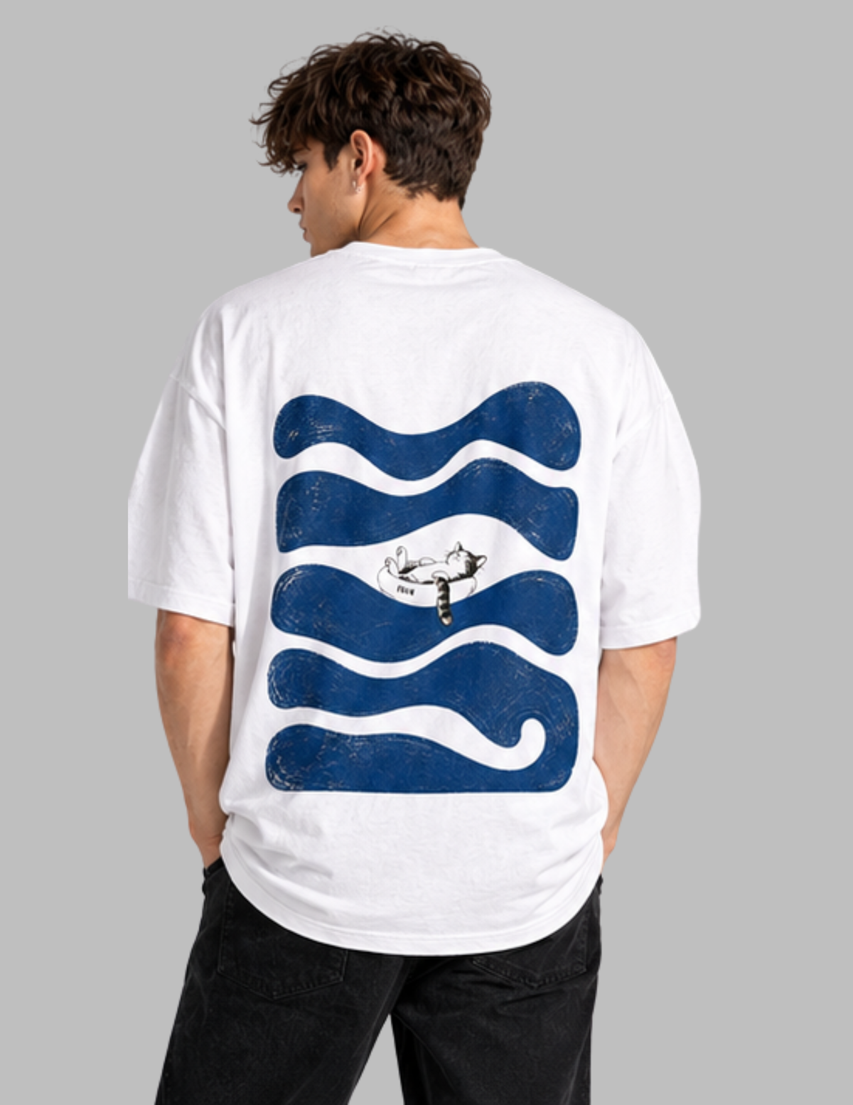 A man wearing a white oversized t-shirt from the back, featuring a large graphic of wavy blue lines with a central black and white mountain and deer design, set against a solid gray background.