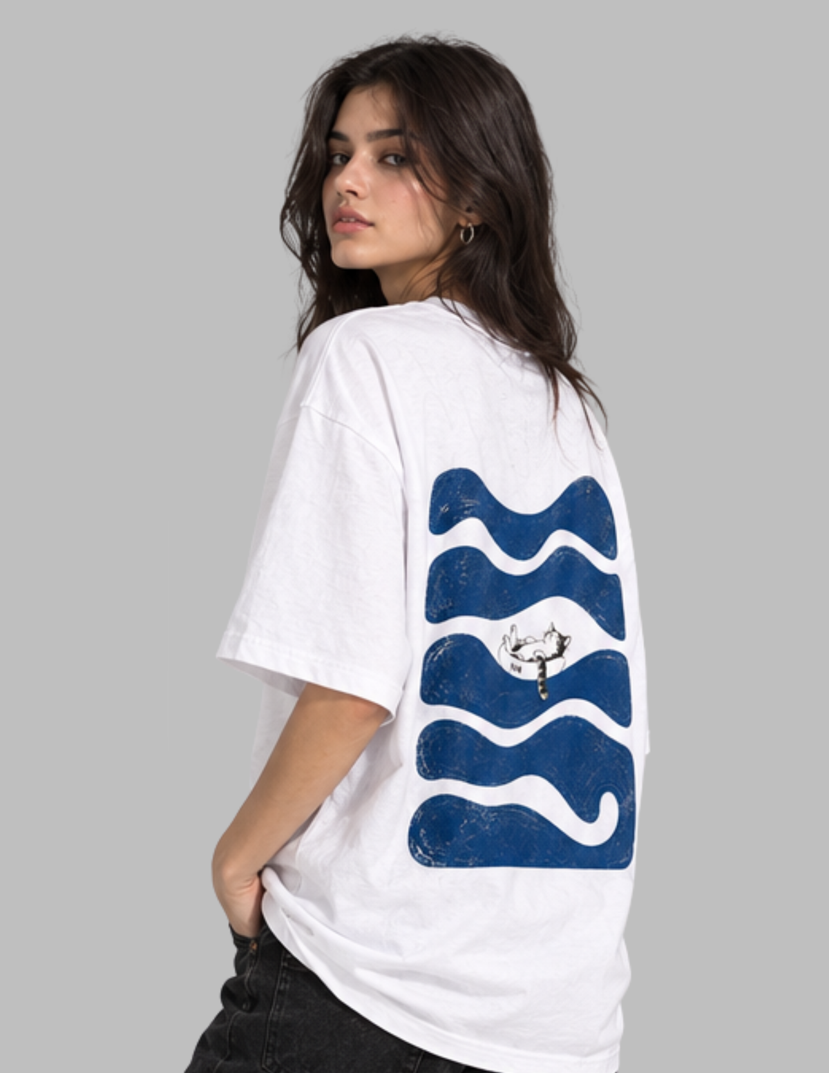 A woman wearing an oversized white t-shirt with a large blue wavy graphic print on the back, shown from a three-quarters angle against a solid gray background.