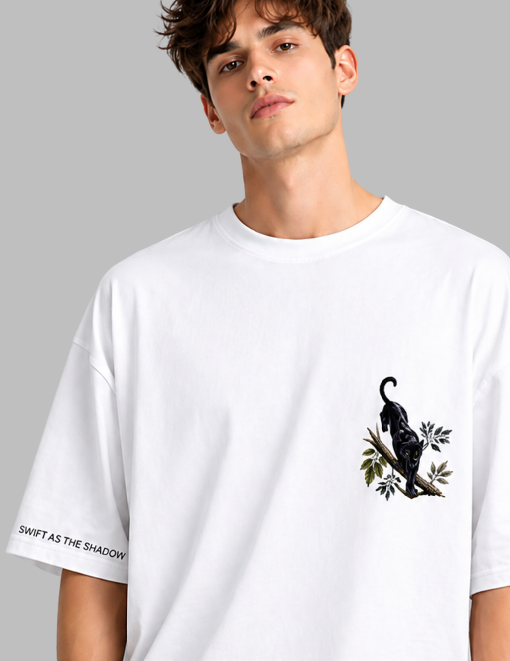A white oversized crewneck t-shirt with a black panther graphic on the left chest and 'SWIFT AS THE SHADOW' text on the right sleeve, modeled by a young man against a solid gray background.