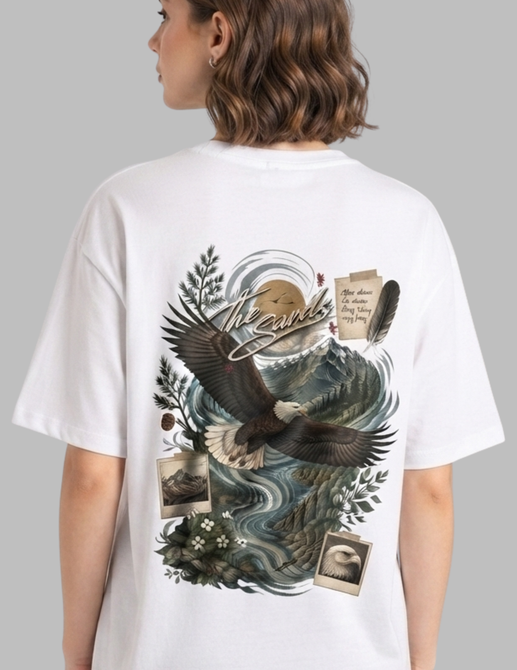 A woman shown from the back wearing an oversized white graphic T-shirt. The shirt features a large detailed print of an eagle over mountains and water, with vintage-style photo frames, a feather, and cursive text reading 'The Wild'.