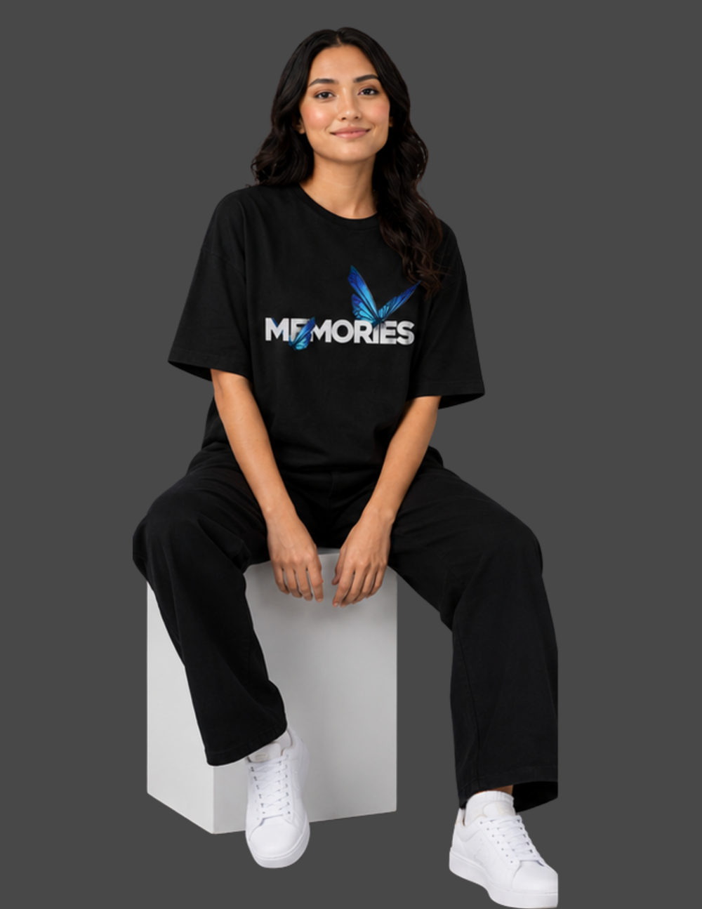 Person wearing a black 'MEMORIES' t-shirt sitting on a white block against a gray background