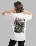 A woman shown from the back wearing a white short-sleeve T-shirt with a large detailed graphic print on the back featuring an eagle, waves, and parchment, paired with black pants against a solid gray background.