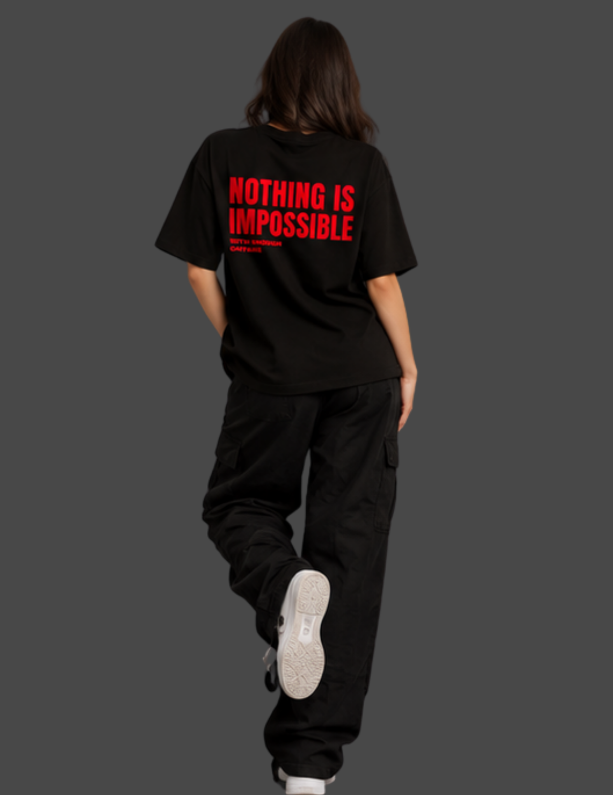 A person shown from the back wearing an oversized black T-shirt with bold red text reading 'NOTHING IS IMPOSSIBLE' and black cargo pants against a dark gray studio background.