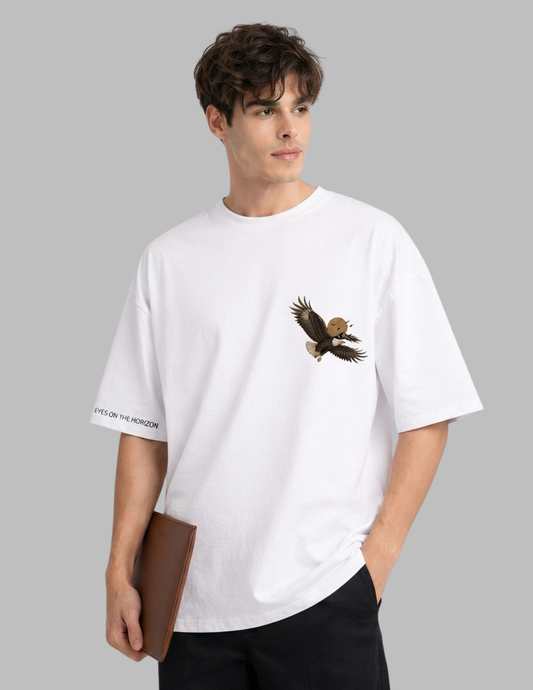 A man wearing a white oversized crewneck t-shirt with a graphic of a flying bald eagle on the left chest and black text on the right sleeve, set against a solid gray background.