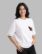 A woman wearing a white oversized t-shirt with a brown eagle graphic on the left chest and 'FISH ON THE WATER' printed on the right sleeve, set against a solid gray background.