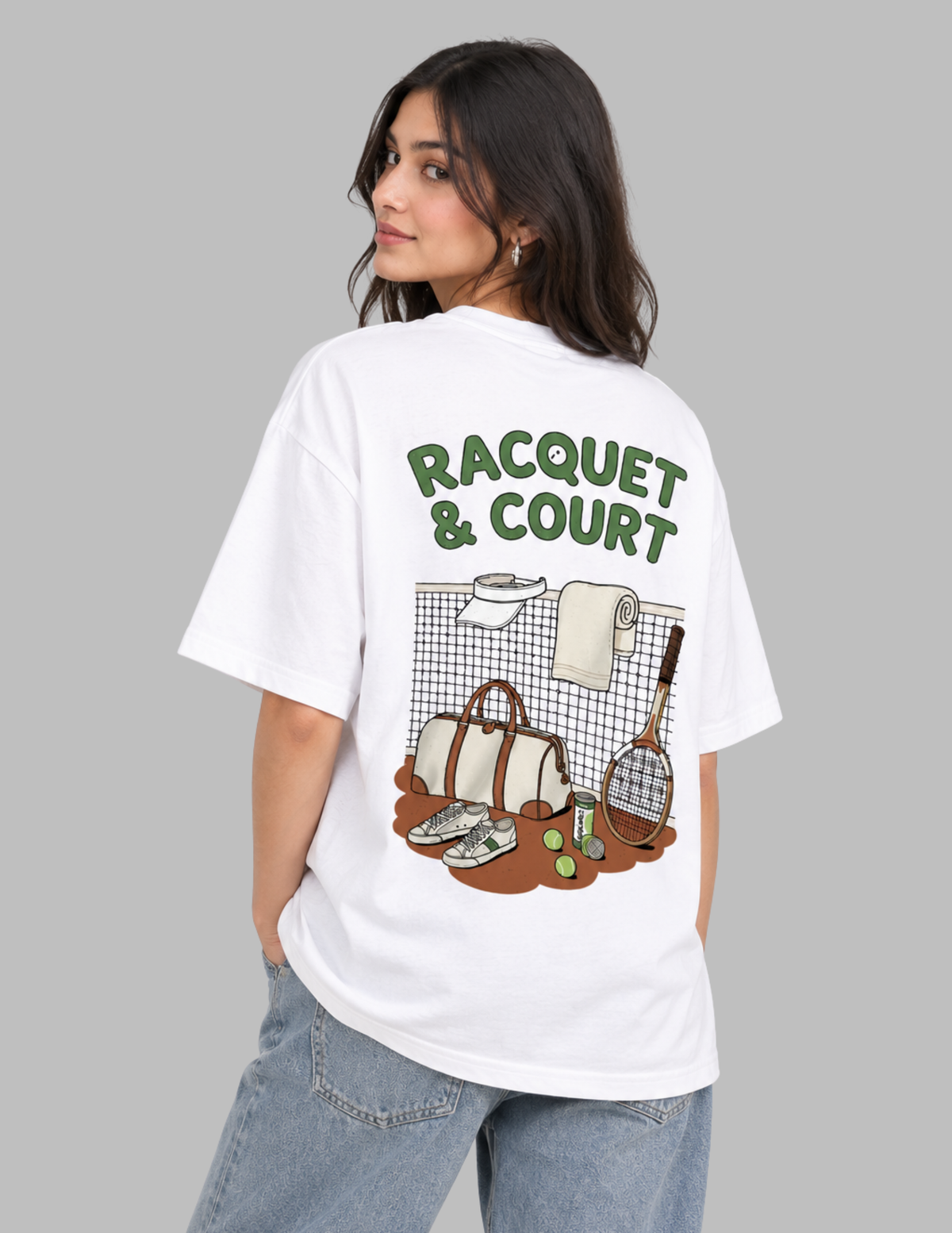 A woman wearing a white oversized graphic t-shirt with a green and brown 'RACQUET & COURT' design on the back, paired with light blue jeans, set against a solid gray background.