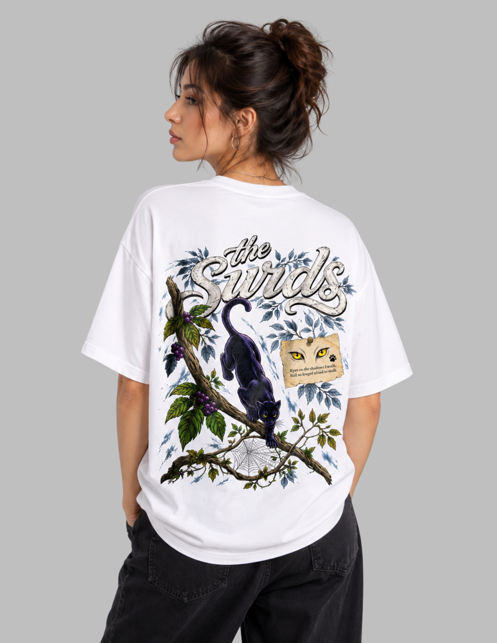 A woman shown from the back wearing a white oversized graphic T-shirt with a large printed design featuring a black bird on a branch, blue leaves, and the text 'The Swirls,' against a plain light gray background.