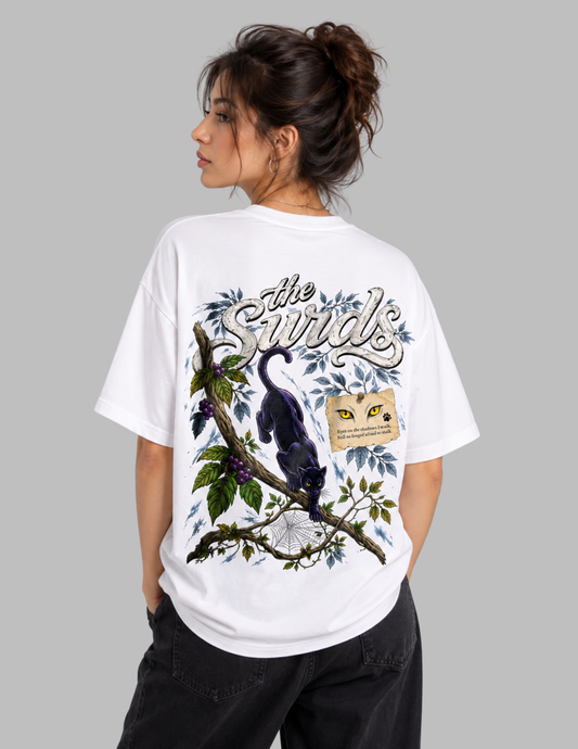 A woman shown from the back wearing a white oversized graphic T-shirt with a large printed design featuring a black bird on a branch, blue leaves, and the text 'The Swirls,' against a plain light gray background.