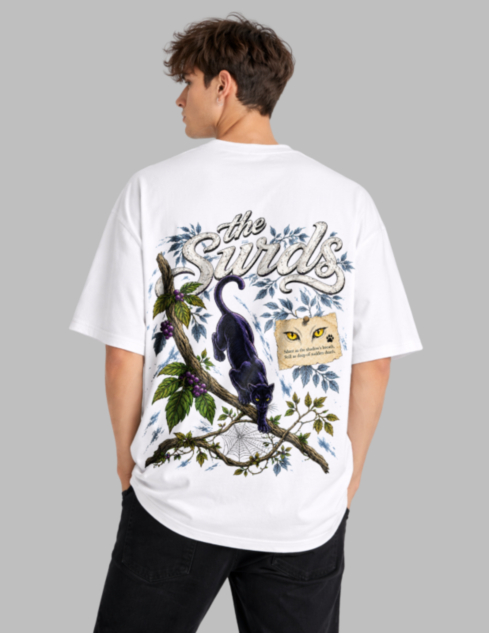 A man wearing a white oversized t-shirt with a large graphic print on the back, featuring a black cat, a spiderweb, and the text 'The Swirlds'.