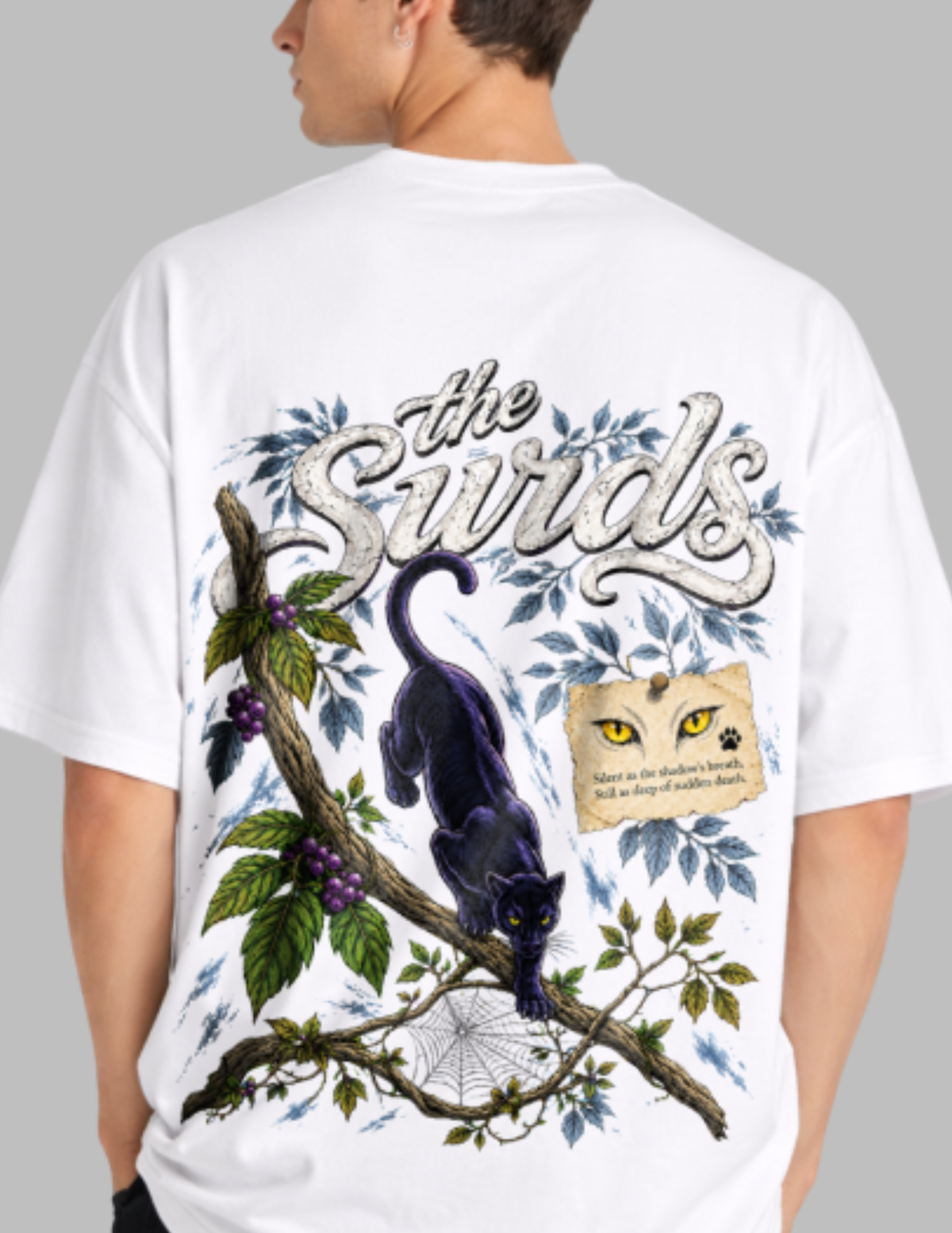 A man wearing a white t-shirt, viewed from the back. The shirt features a large graphic print with the text 'the Swirlds' in a stylized font, a black cat on a tree branch with green leaves and purple berries, a spiderweb, and a small illustrated face with yellow eyes and the text 'Name the sun's tears, and we shall find them again.