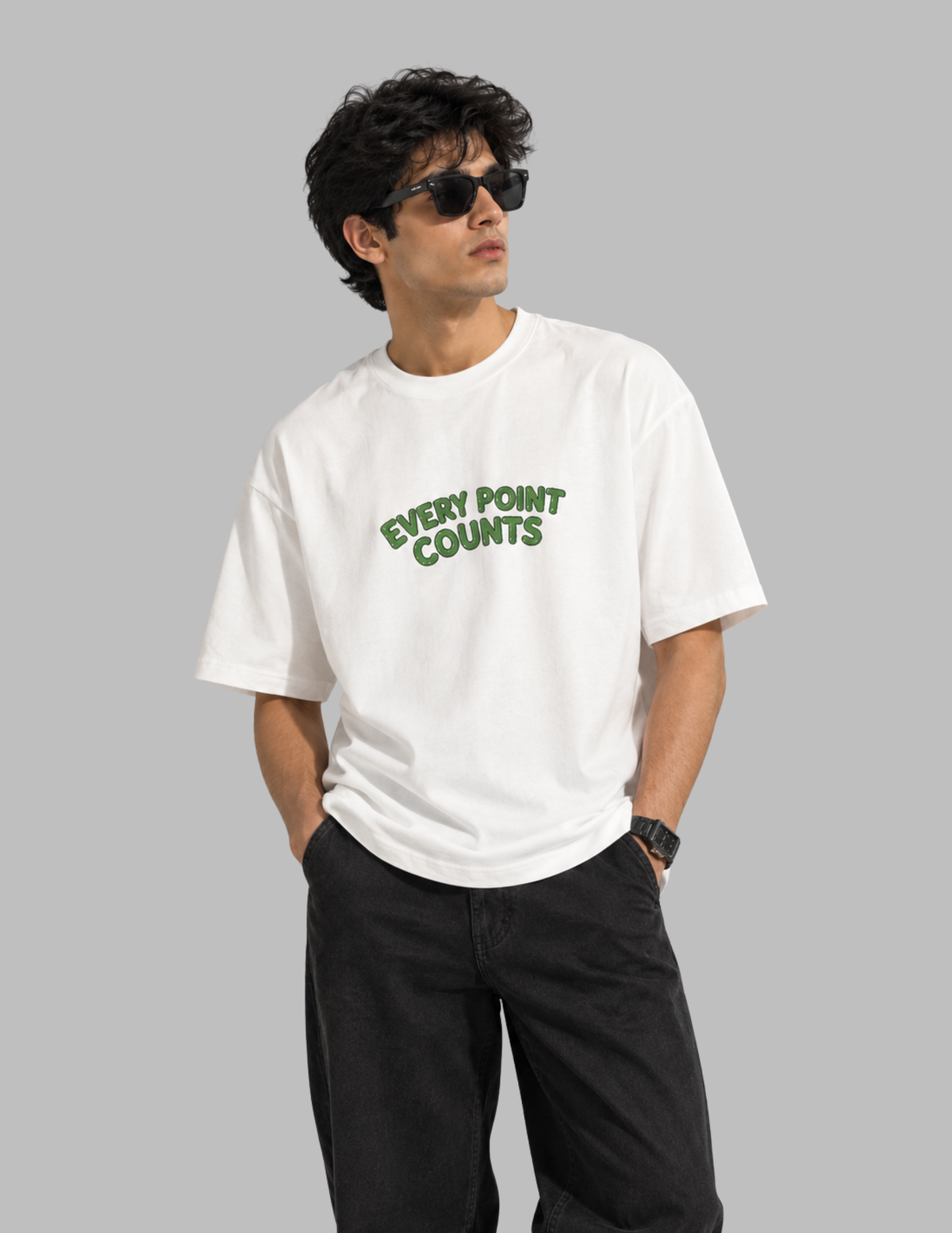 A man wearing a white crewneck t-shirt with the phrase 'EVERY POINT COUNTS' printed in green across the chest, paired with black pants and sunglasses, set against a solid gray background.