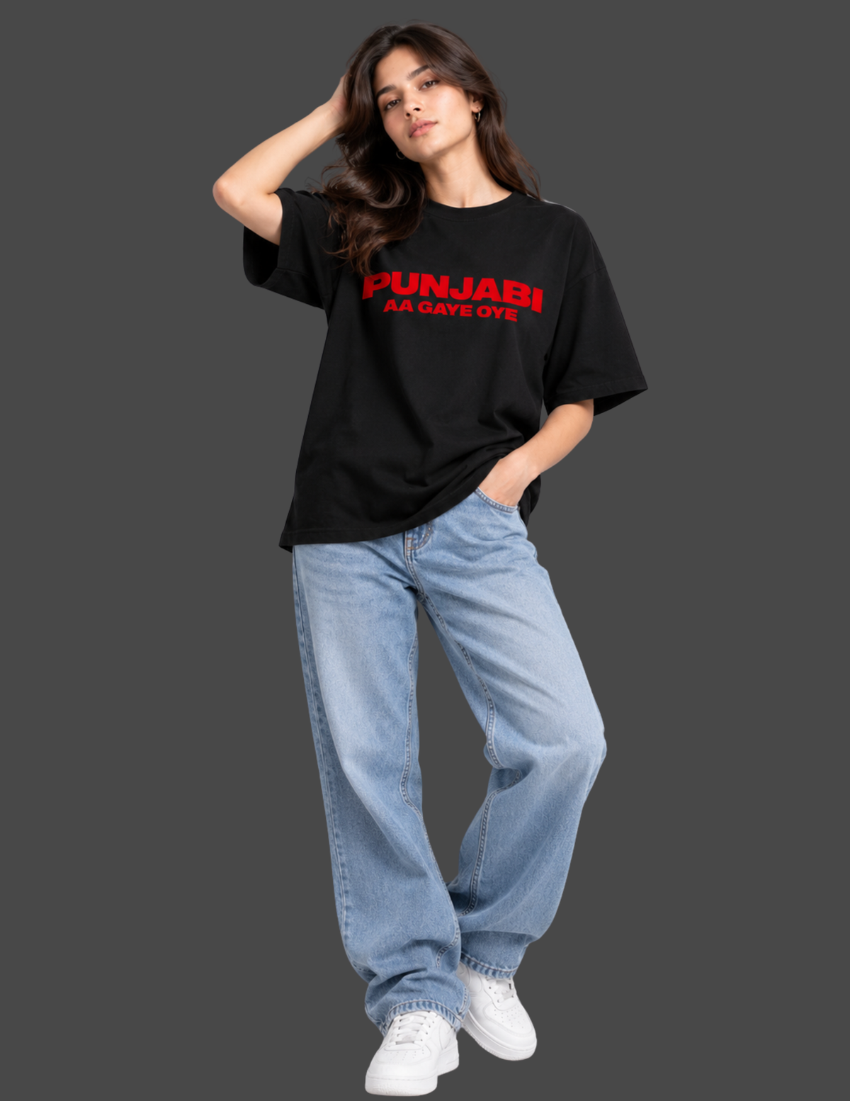 A woman modeling a black oversized graphic T-shirt with red text reading 'PUNJABI 66 DAYS OYE' on the chest, paired with light blue jeans and white sneakers, against a dark gray studio background.