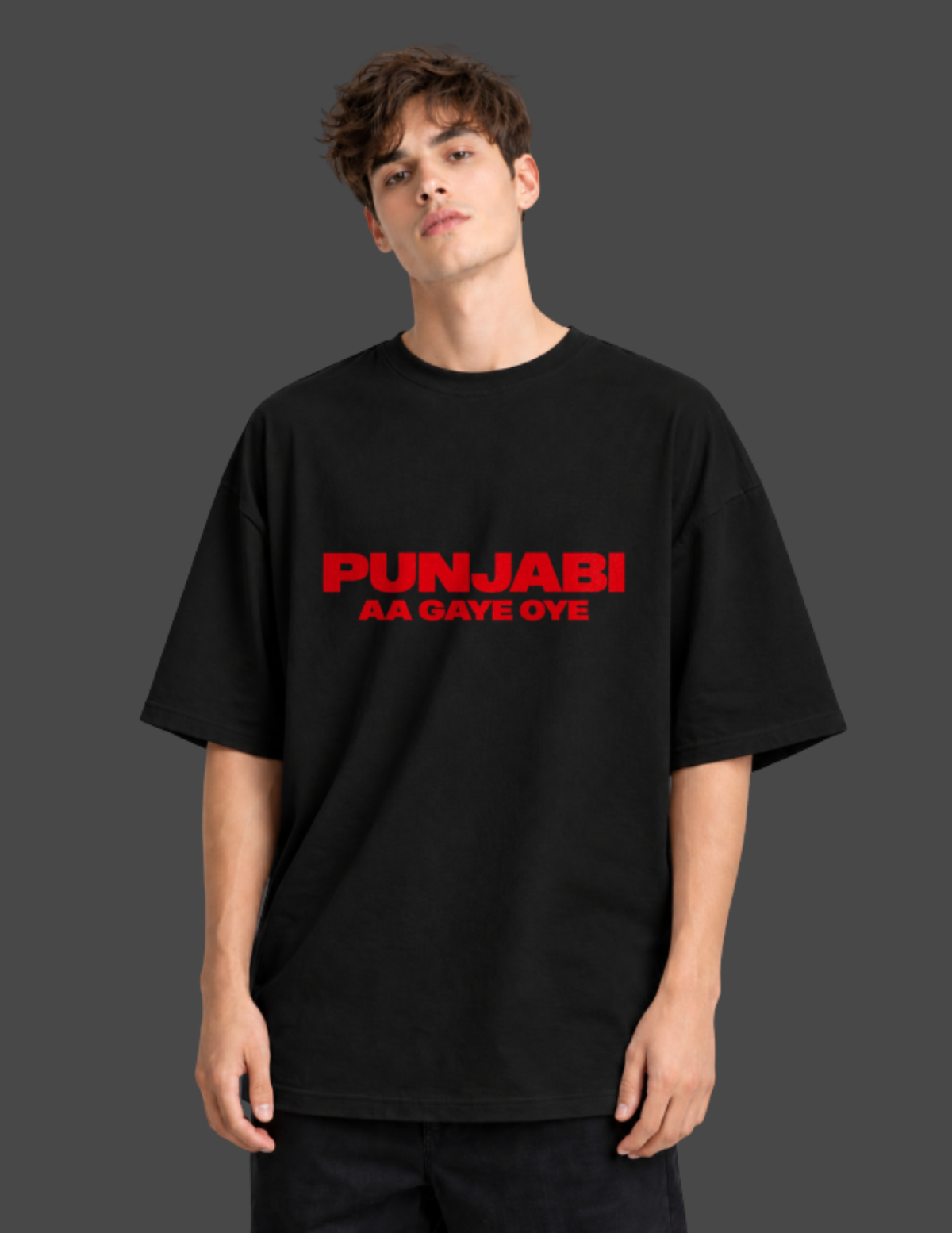 A man wearing an oversized black t-shirt with red text reading 'PUNJABI AA GAVE OYE' on the chest, set against a dark gray background.