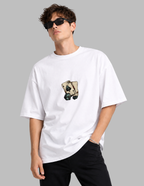 A man wearing a white oversized t-shirt with a graphic of two playing cards on the chest, styled with black pants and sunglasses against a solid gray background.