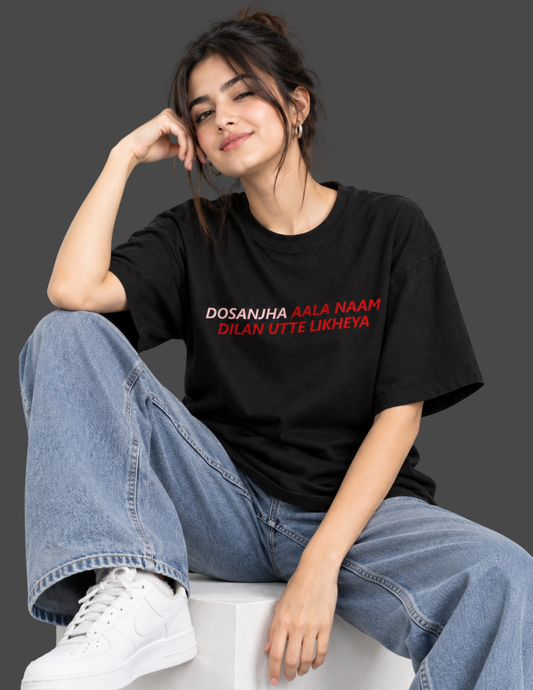 A woman sitting on a white block wearing a black graphic t-shirt with red and white text, blue jeans, and white sneakers against a dark gray background.