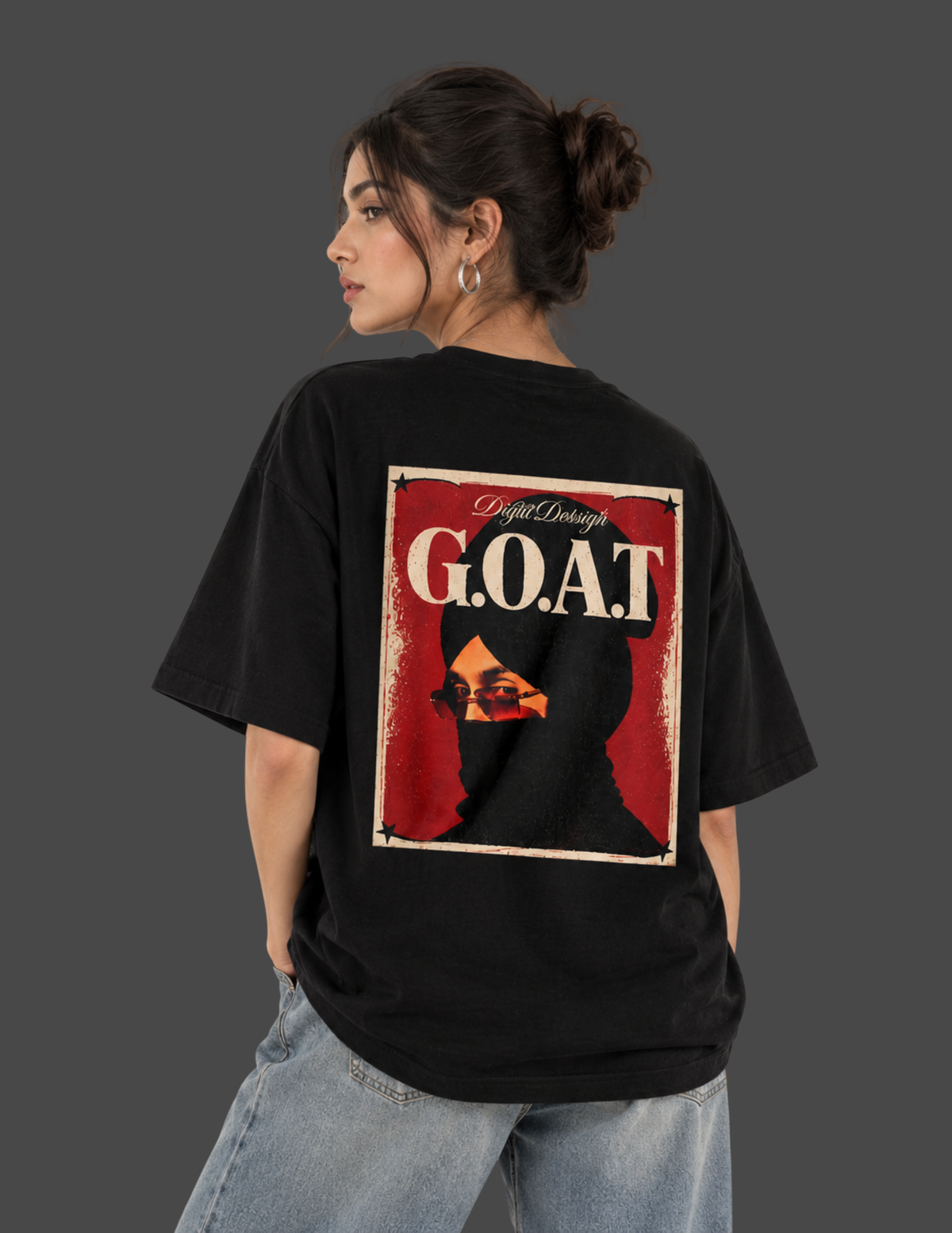 A woman wearing a black oversized t-shirt with a large graphic print on the back, sitting on a concrete block against a dark gray studio background.