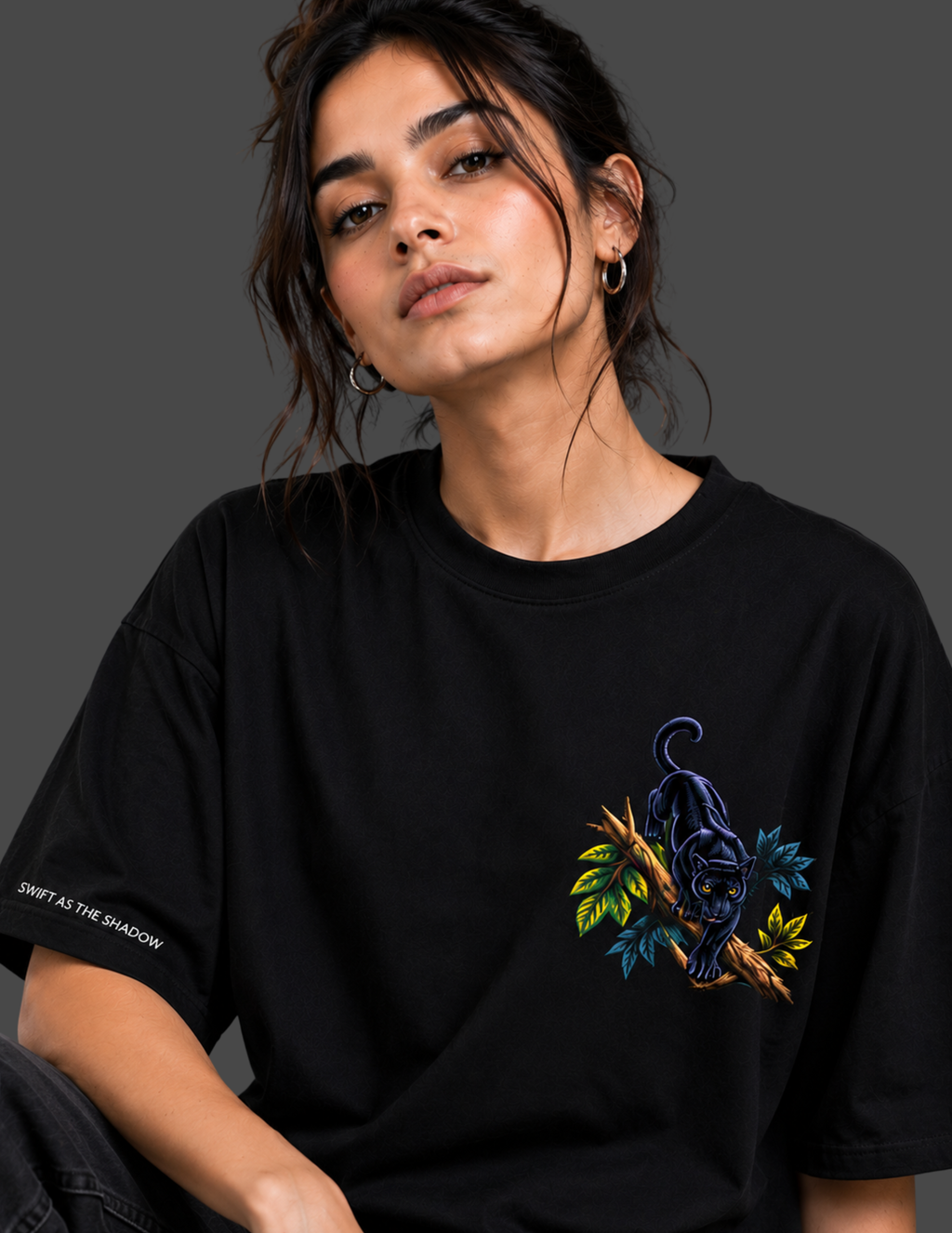 A woman wearing a black short-sleeve t-shirt with a colorful graphic of a panther on a branch with green and blue leaves. The t-shirt also features white text on the sleeve that reads 'SHIRT AS THE SHADOW'.