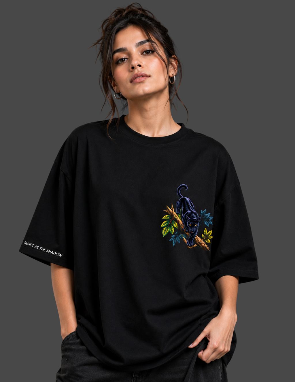 A woman wearing an oversized black t-shirt with a colorful panther graphic on the chest and white text on the sleeve, set against a dark gray studio background.