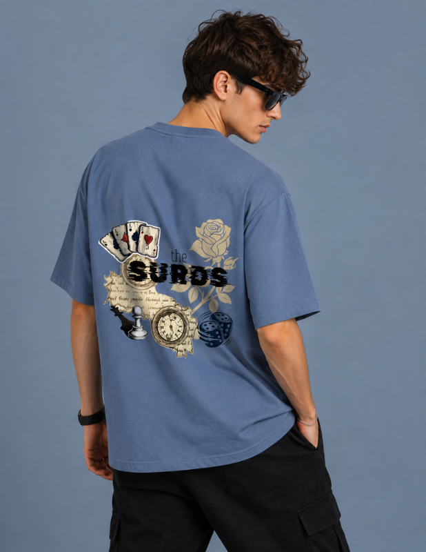 A man wearing a faded blue t-shirt with a large graphic print on the back, featuring playing cards, a rose, a clock, and the word 'SURODS'.