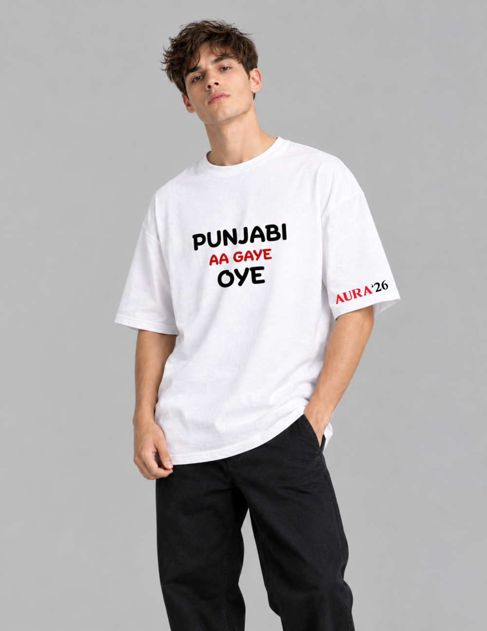 A man modeling a white short-sleeve graphic t-shirt with black and red text reading 'PUNJABI AA GAYE OYE' on the chest and 'ALRA'26' on the sleeve, paired with black pants against a solid gray background.