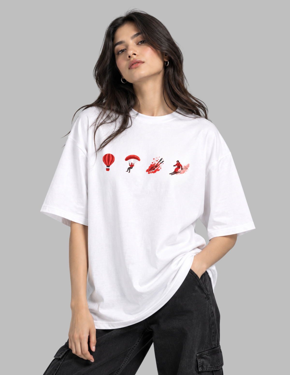 A woman wearing an oversized white t-shirt with a red graphic print of parachutist silhouettes, paired with black cargo pants, against a solid gray background.