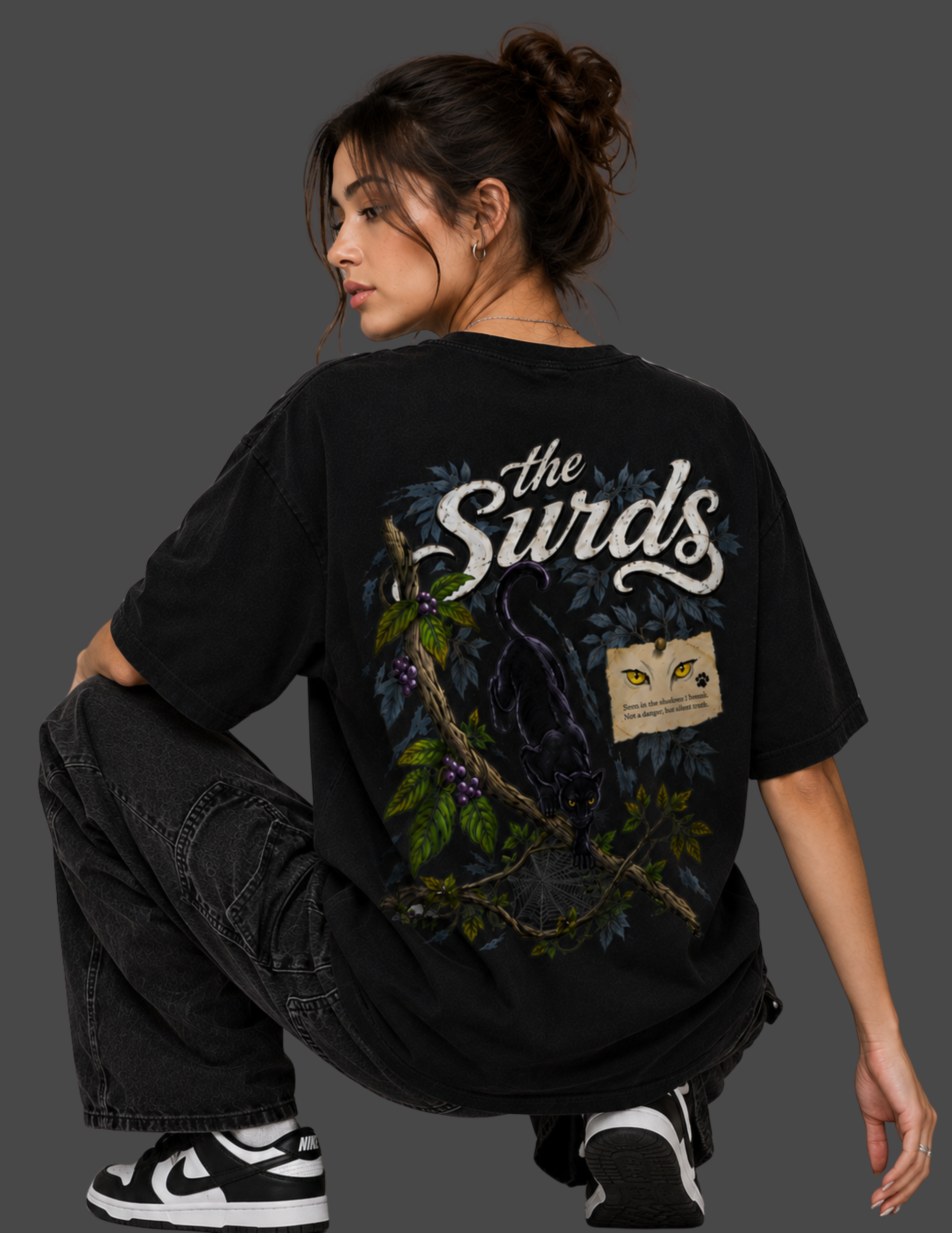 A model wearing a black graphic t-shirt with a large back print featuring the text 'the Surds' and a black cat illustration, posed against a dark gray background.