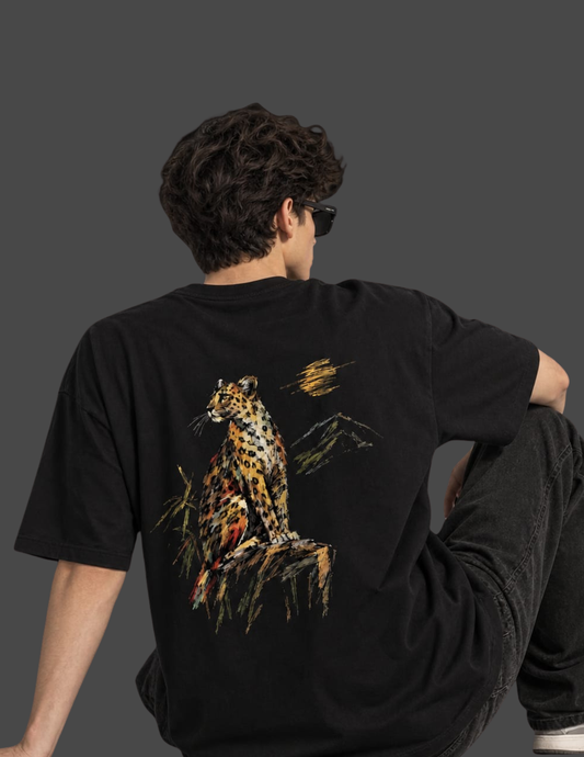 A man wearing a black oversized t-shirt with a large graphic print of a leopard on the back, shown from behind against a dark gray studio background.