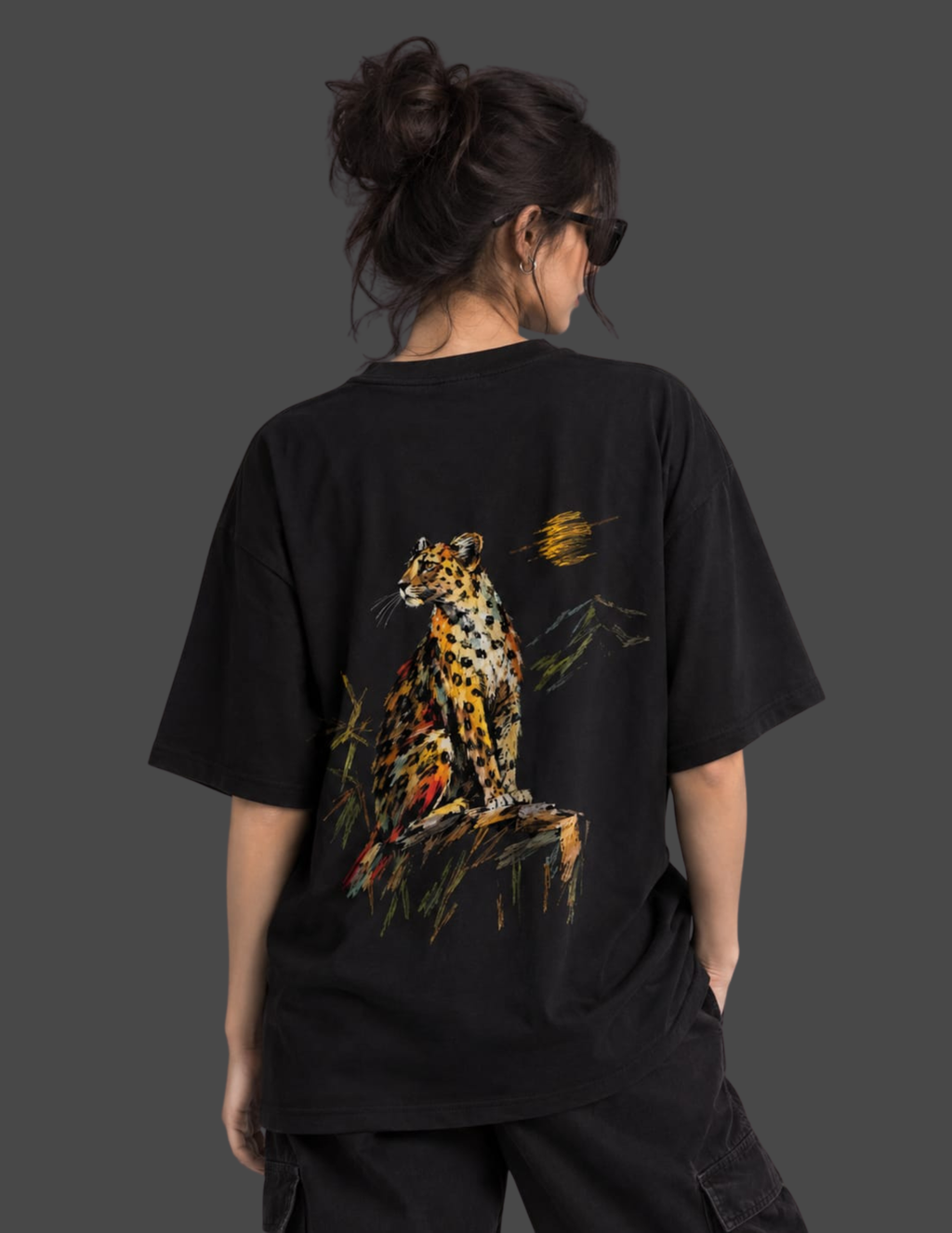 A person shown from the back wearing an oversized black T-shirt with a large colorful leopard graphic on the back, photographed against a dark gray studio background.