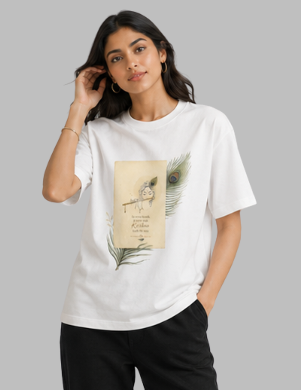 A woman modeling a white short-sleeve t-shirt with a vintage-style graphic print featuring a peacock feather and a bird illustration on the front, paired with black pants against a solid gray background.