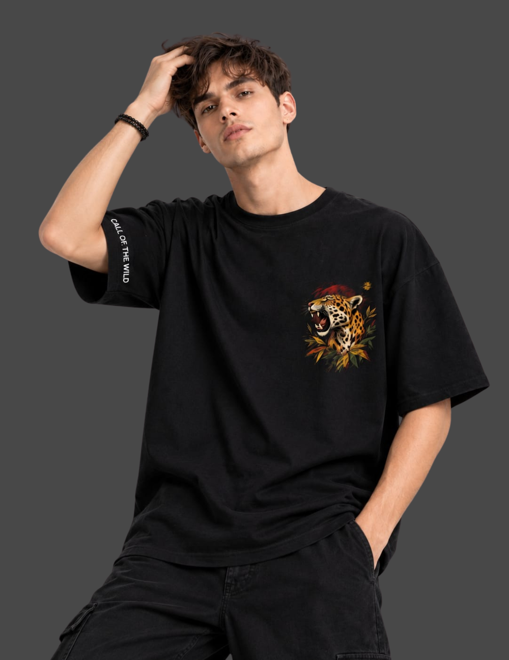 A man wearing a black oversized t-shirt with a colorful leopard graphic on the left chest and white text on the right sleeve, posed against a dark gray studio background.