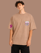Man wearing a beige t-shirt with a logo and number on a brown background