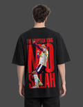 Person wearing a black t-shirt with a graphic and text on the back, on a plain background