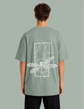 Person wearing a green t-shirt with a white dragonfly design on the back against a gray background