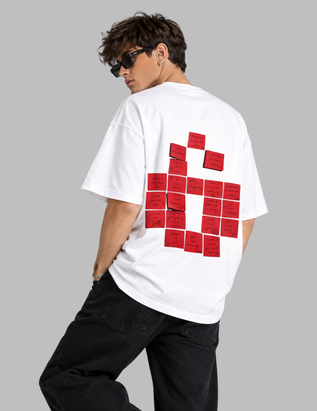 A man wearing a white oversized T-shirt with a large red graphic made of rectangular blocks on the back, paired with black pants and sunglasses, photographed against a plain light gray studio background.