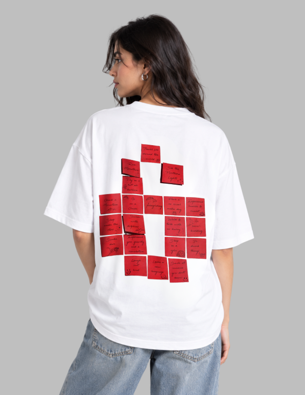 A woman shown from the back wearing an oversized white T-shirt with a large graphic of red sticky notes on the back, paired with light blue jeans, against a solid gray background.