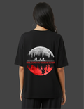 Person wearing a black t-shirt with a graphic design on the back, featuring a moon and silhouette of a forest.