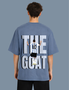 Person wearing a blue t-shirt with 'The Goat' graphic on the back against a gray background