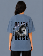 Person wearing a blue t-shirt with 'OLISE' and 'MICHAEL' printed on the back against a gray background
