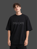 Person wearing a black t-shirt with 'DELICATE' text on a dark background