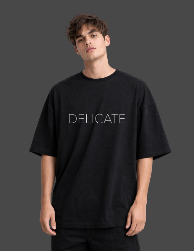 Person wearing a black t-shirt with 'DELICATE' text on a dark background