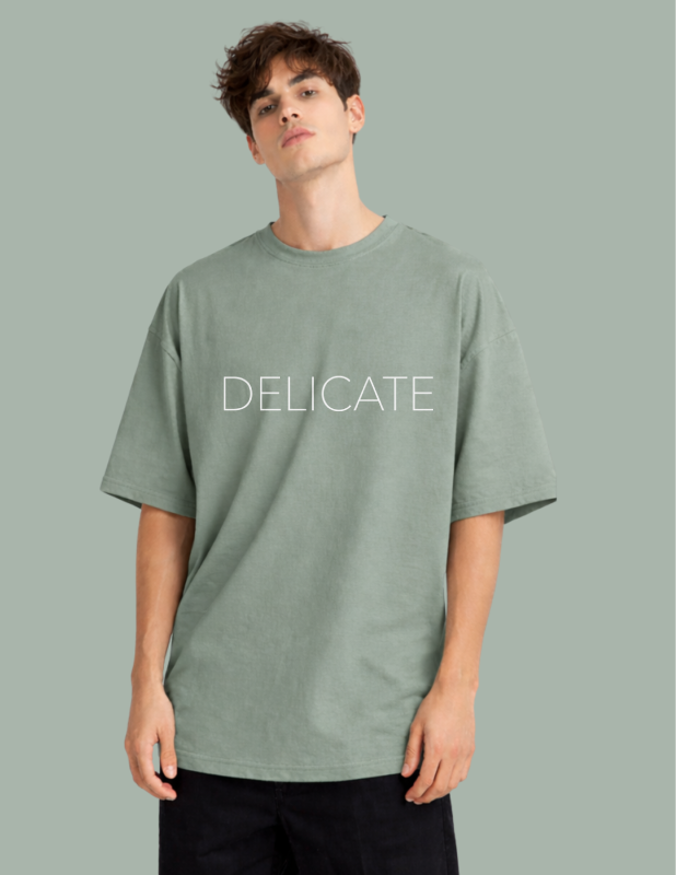 Person wearing a green t-shirt with 'DELICATE' text on a gray background