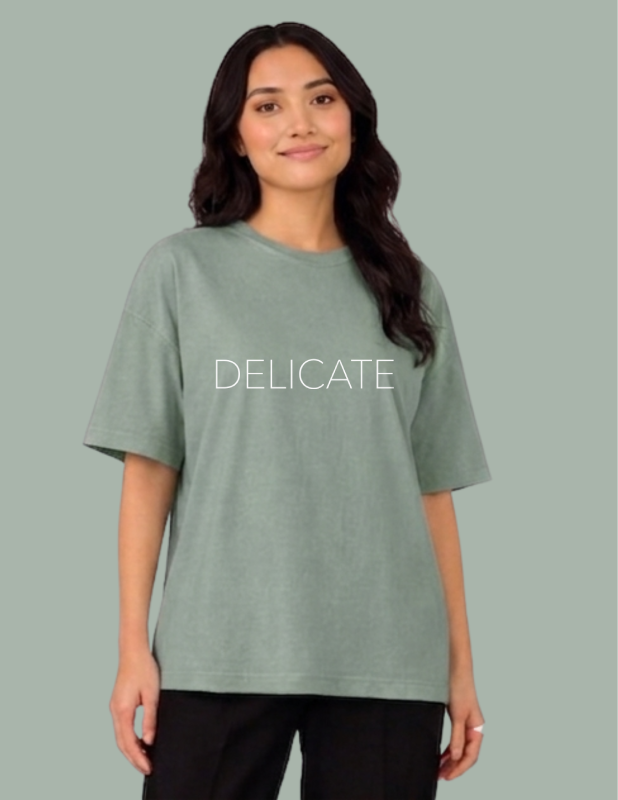 Person wearing a green t-shirt with 'DELICATE' text on a gray background