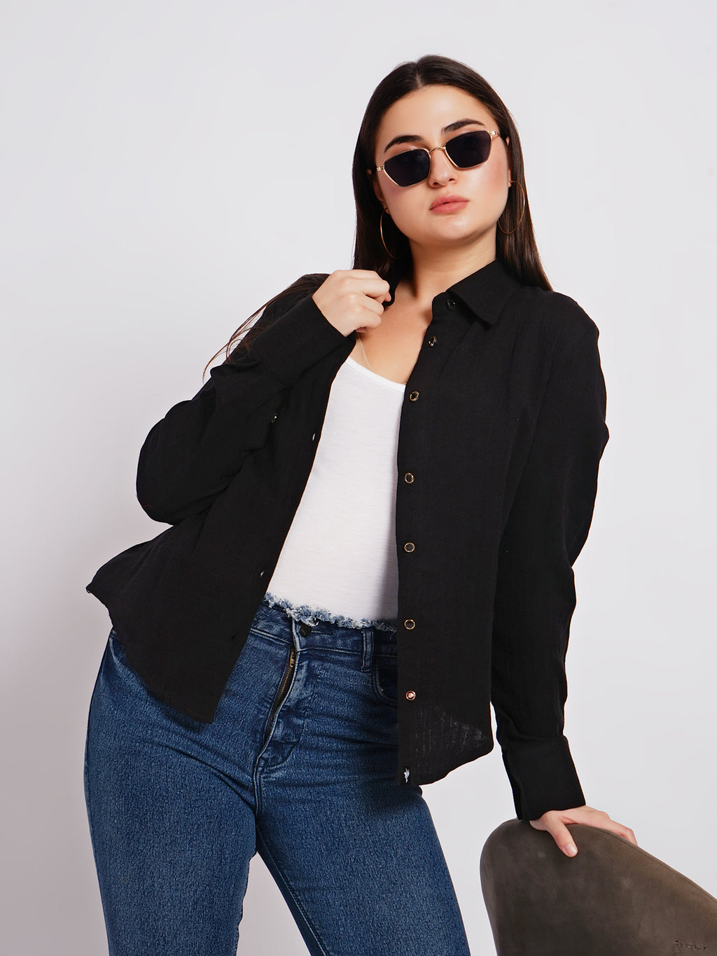 Woman wearing a black jacket, white shirt, and blue jeans against a plain background