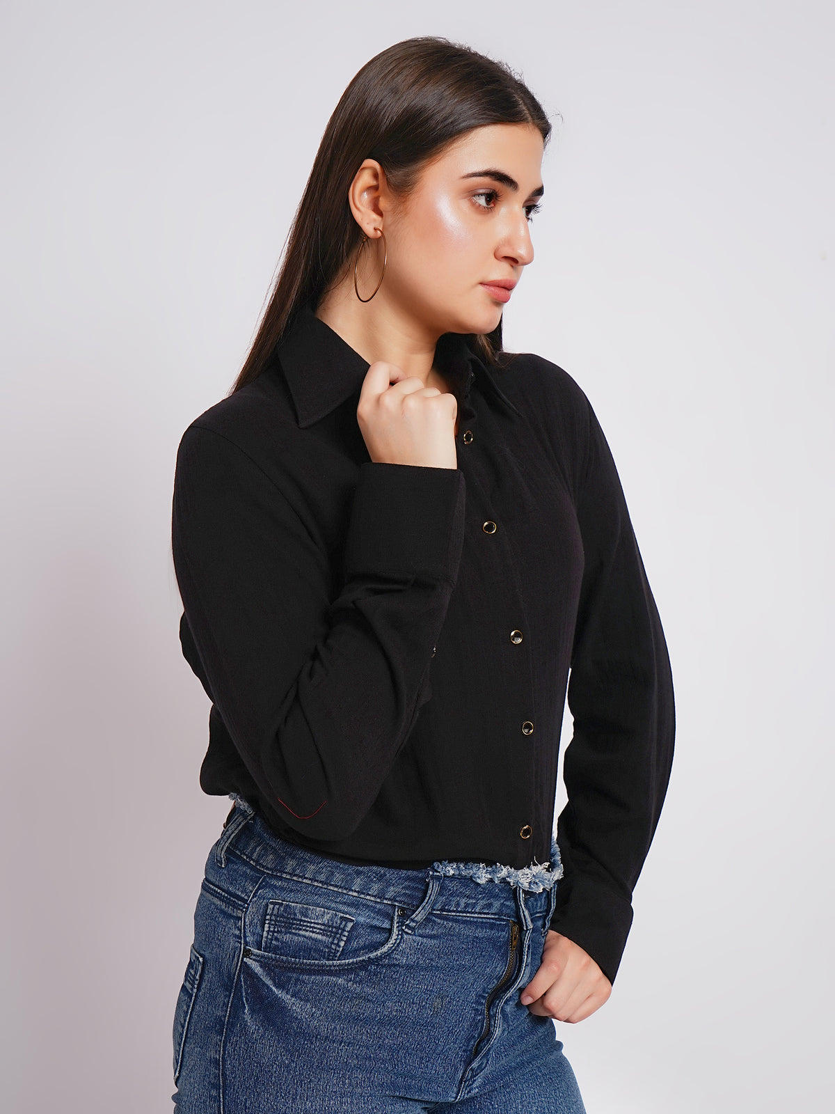Woman wearing a black shirt with gold buttons against a plain background