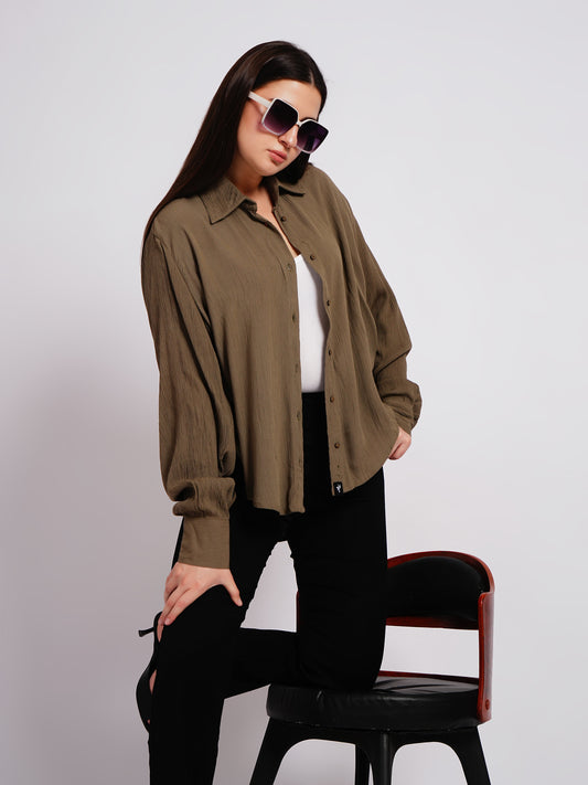 Woman wearing a brown shirt and sunglasses, sitting on a black chair against a white background