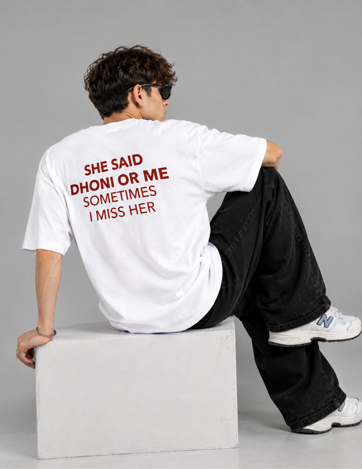 A man wearing a white t-shirt with red text on the back, sitting on a concrete block against a gray studio background.