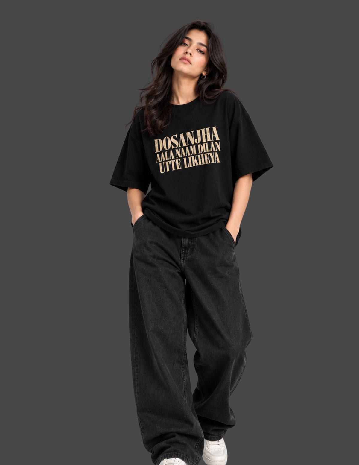 A woman wearing a black oversized t-shirt with a large graphic print on the back, sitting on a concrete block against a dark gray studio background.